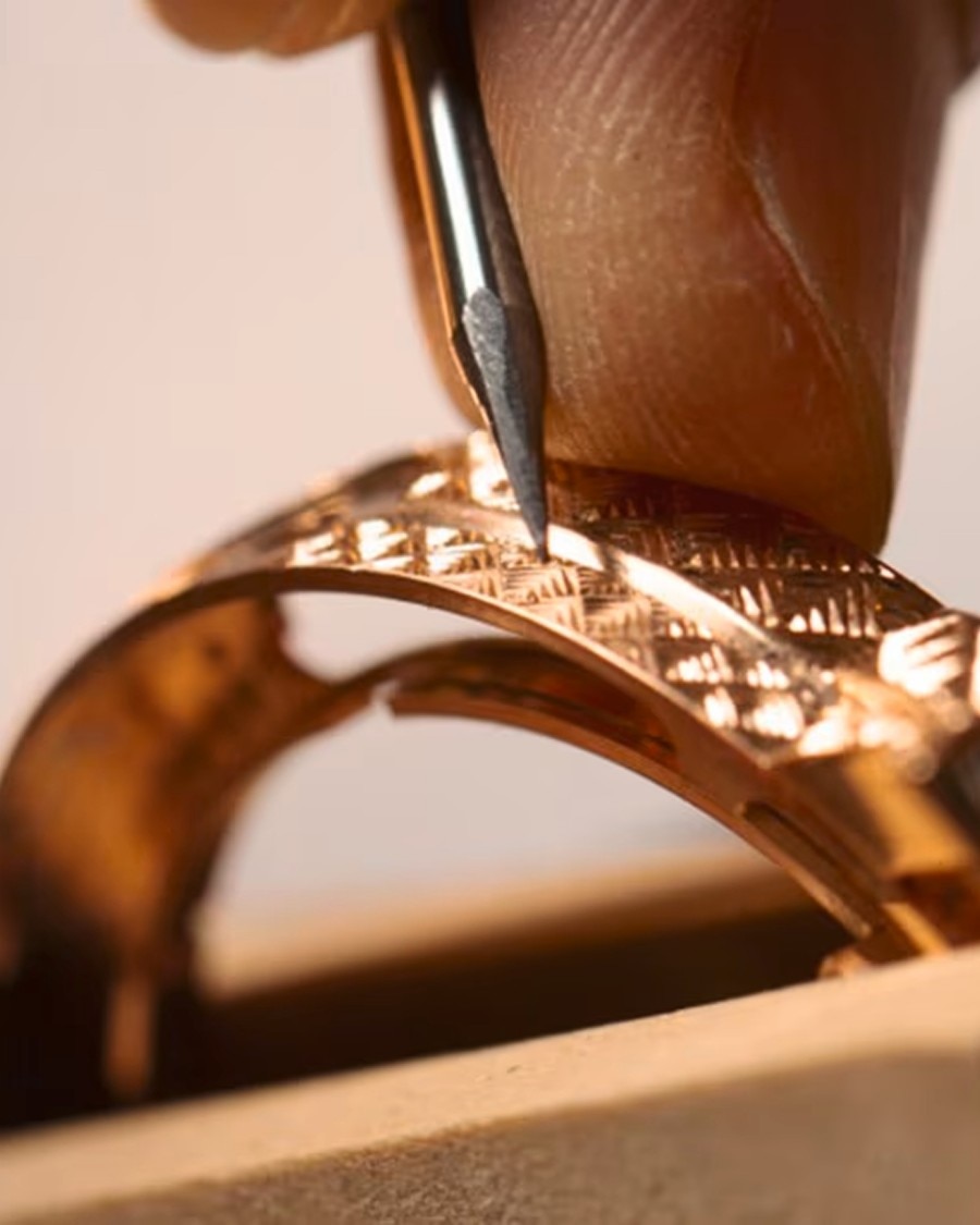 Risorse naturali Detailed view of a hand engraving a decorative pattern onto a golden watch case using a specialized tool.