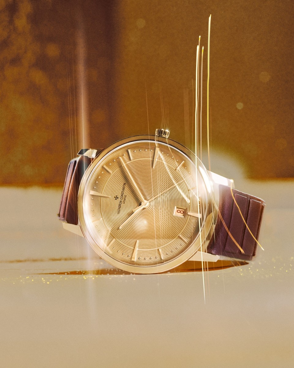 A gold watch with a brown leather strap placed on a reflective golden surface with radiant sparkles.