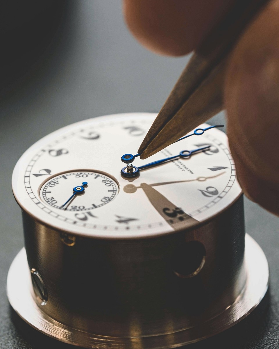 Orologiaio che usa delle pinzette per posizionare le lancette sul quadrante di un orologio.