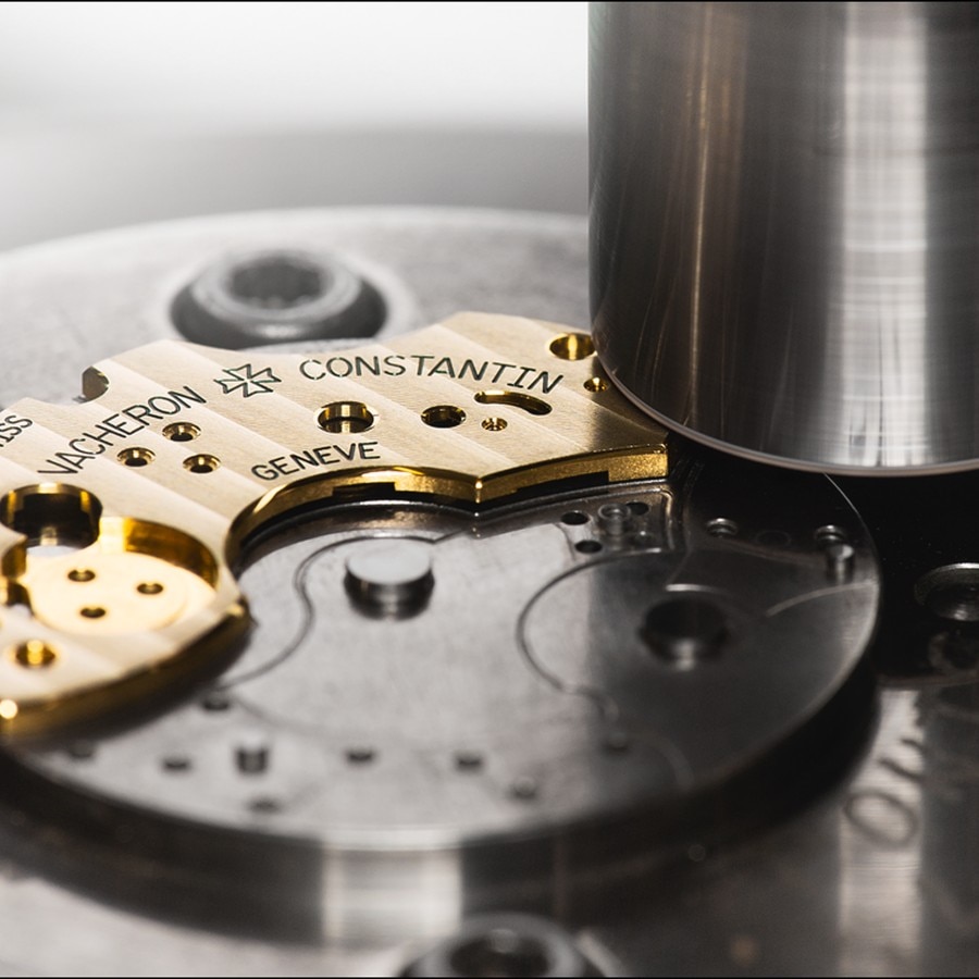 Detailed view of a Vacheron Constantin watch movement plate with engraved markings, positioned under a machine.