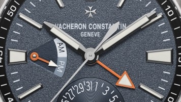 Quadrante di orologio Vacheron Constantin con lancette luminose e dettagli arancioni.