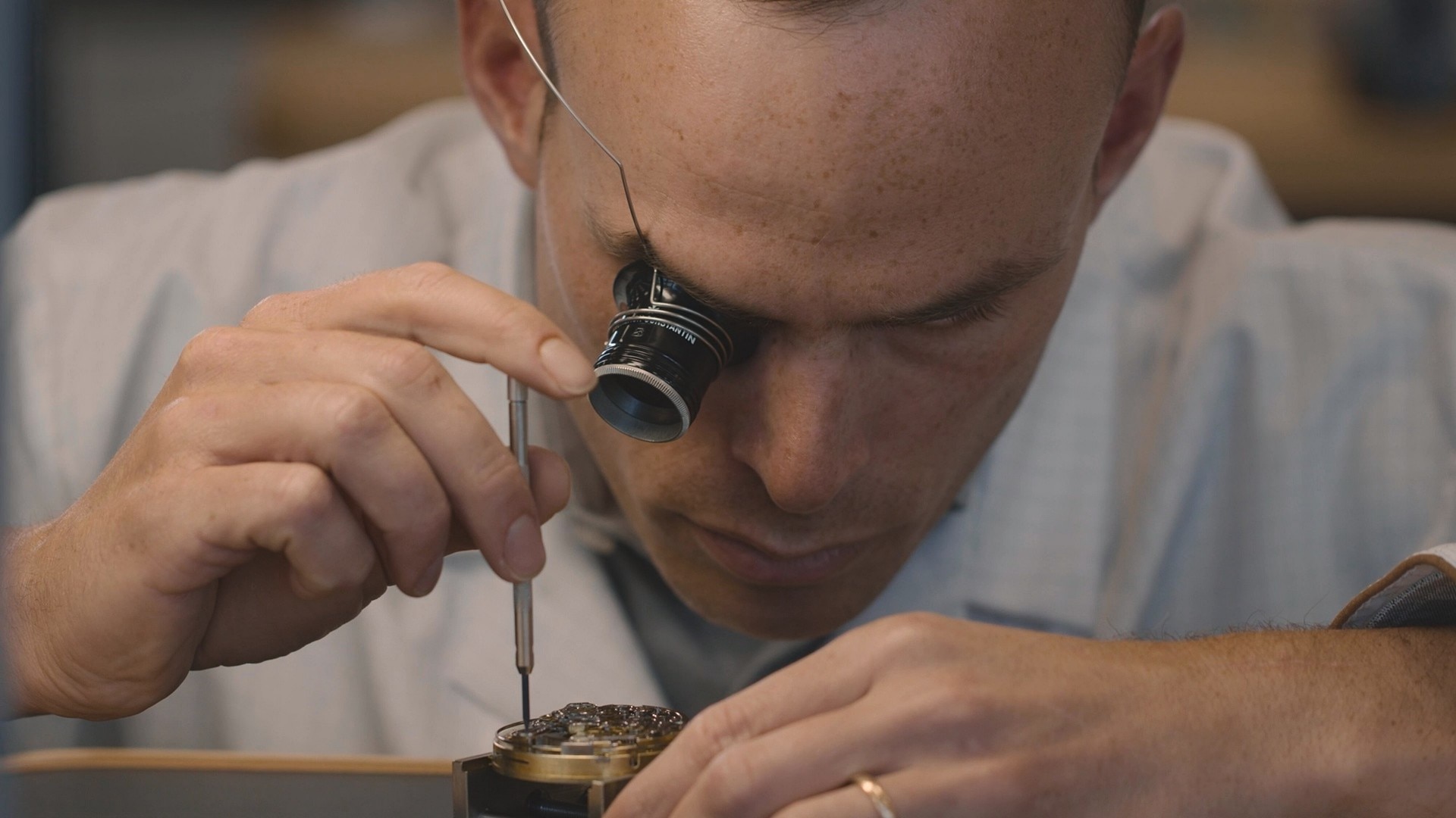 Watchmaker closely inspecting a component through a loupe.