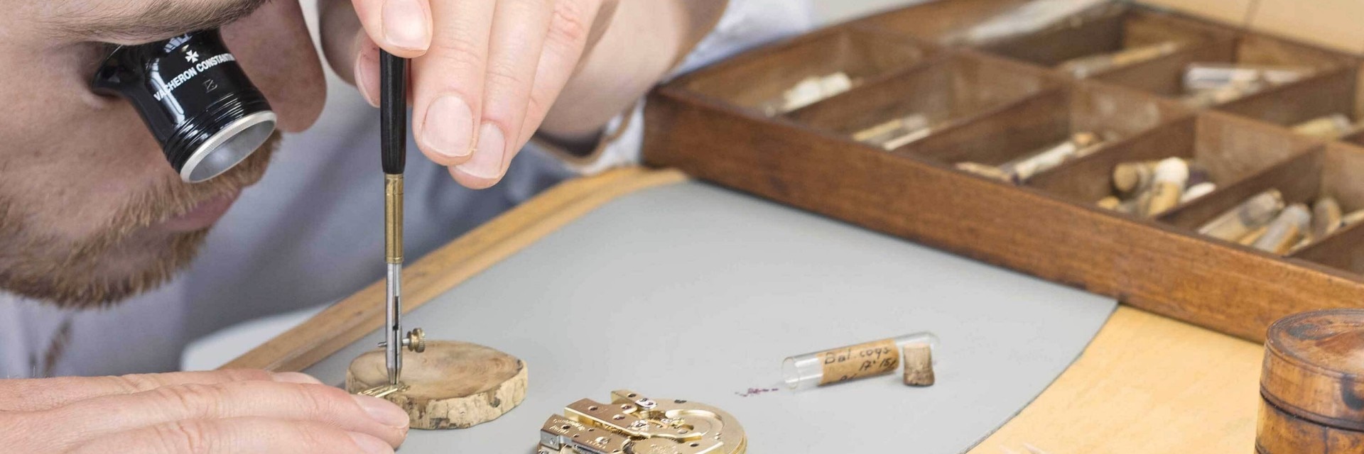 Uhrmacher montiert Uhrenteile mit einem Schraubenzieher an einer Holzwerkbank mit geordneten Werkzeugen.