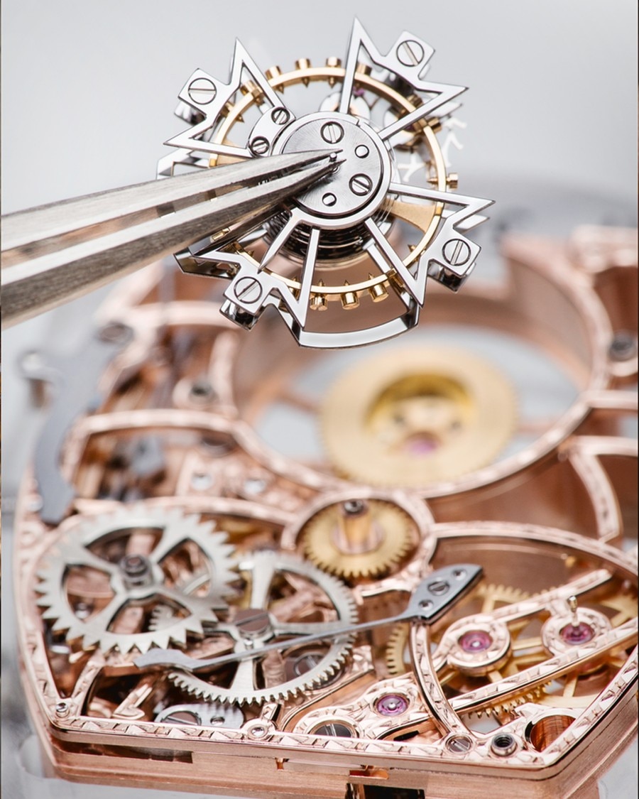 An intricate watch component held by tweezers