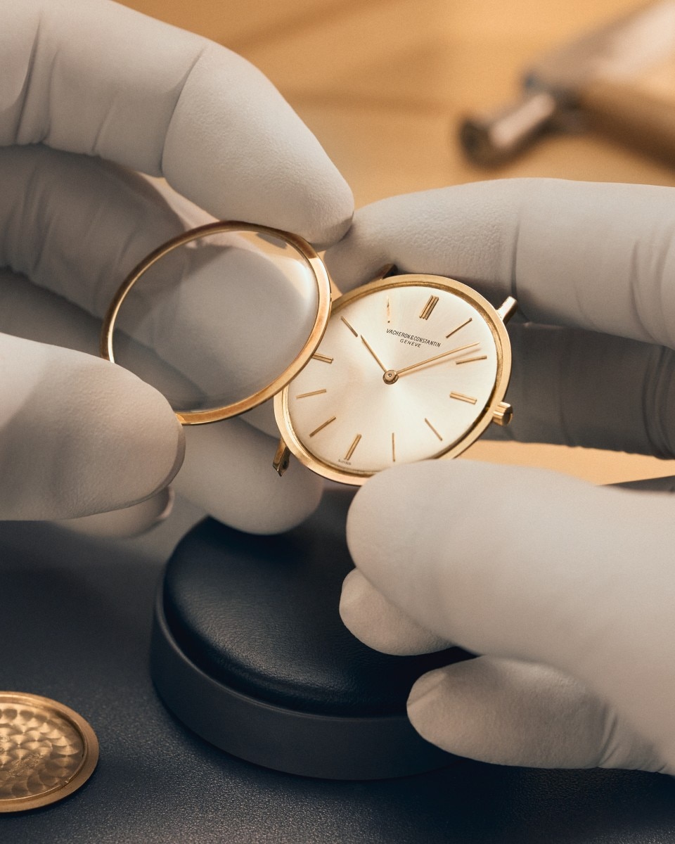 Mani guantate che assemblano un orologio Vacheron Constantin classico con quadrante bianco.