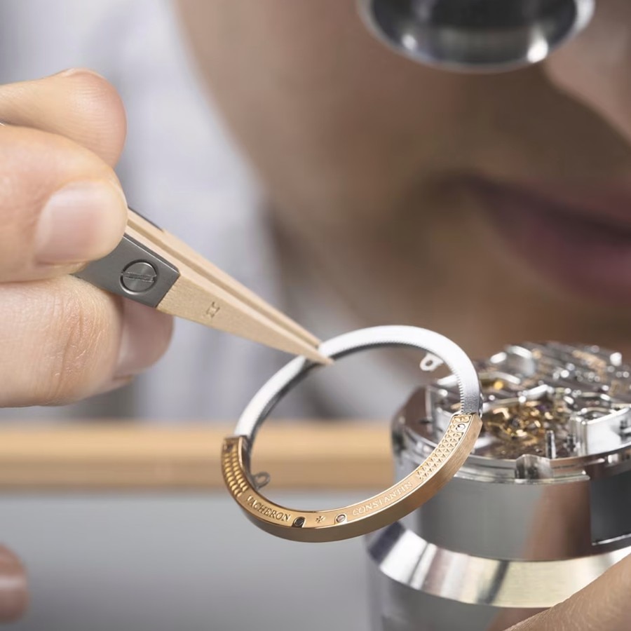 Watchmaker assembling a watch component under a microscope, using precision tweezers and wooden tools.