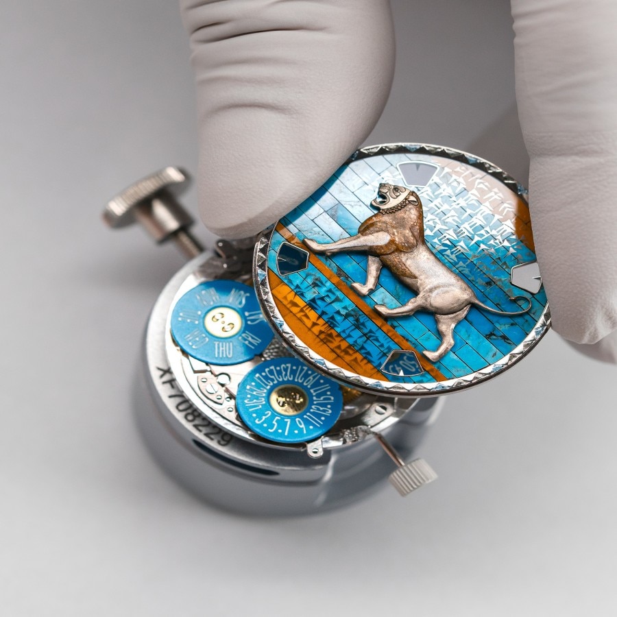 A gloved hand holding a blue watch case back engraved with a lion