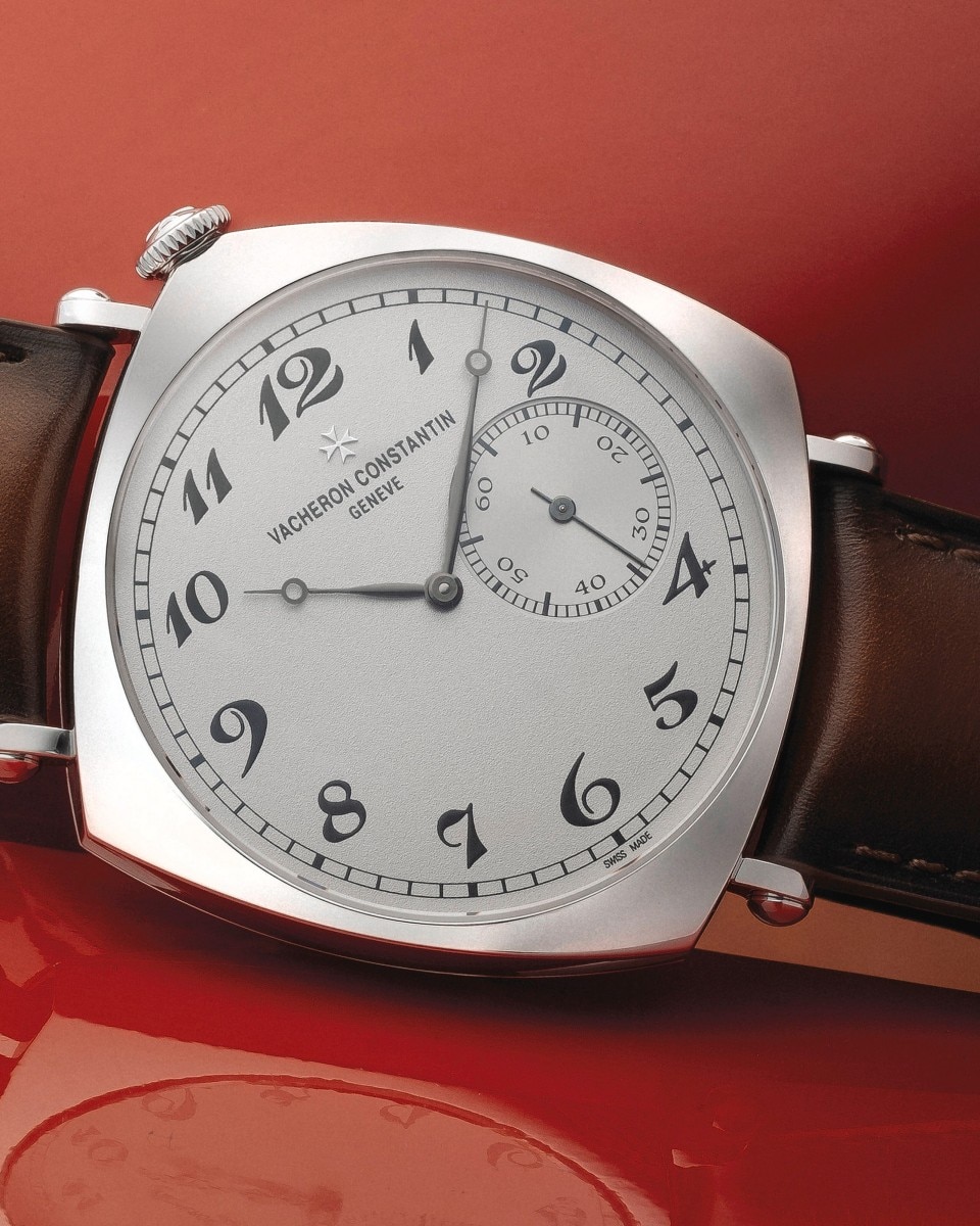 A gold watch with a light dial and brown leather straps on a red background.