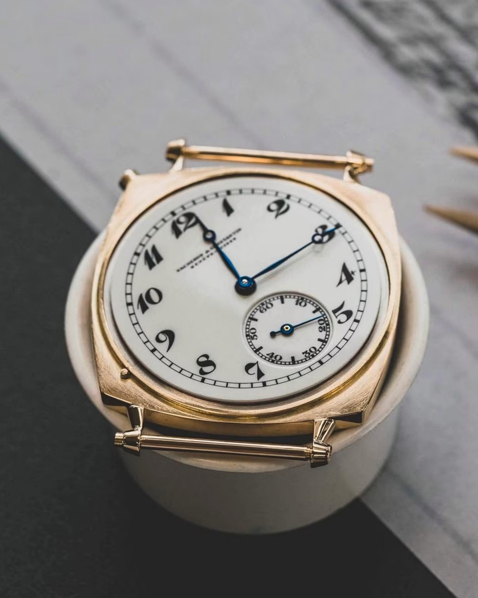 A watch with a light-colored dial, a gold case, and dark numerals and hands.