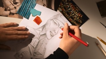 A hand drawing a Athena's head on white paper.