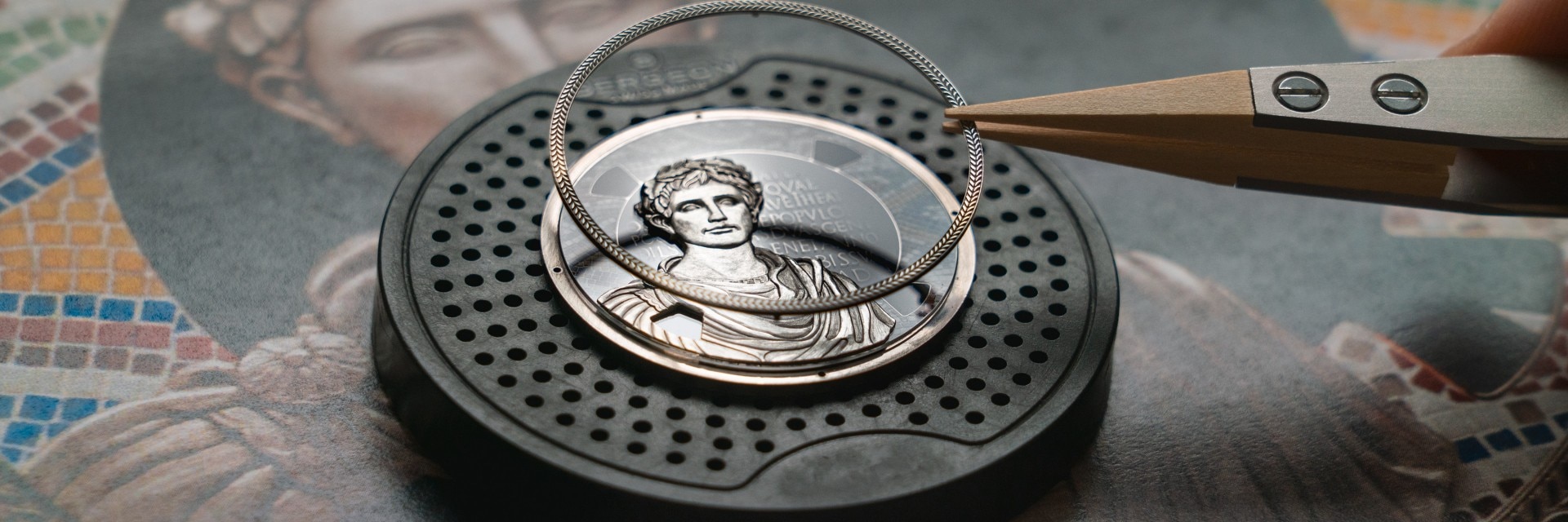 ملاقط تحمل خاتمًا مزخرفًا فوق قرص ساعة مفصل يتميز بتمثال نصفي روماني.