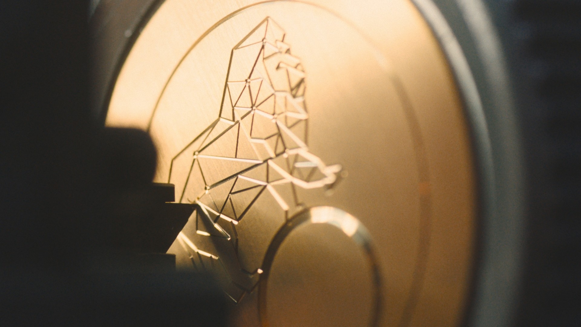 金表部件的特写，带有几何狮子浮雕，部分处于阴影中。