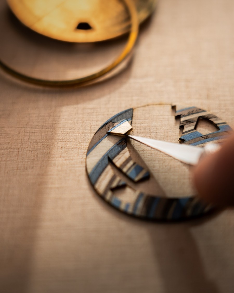 Artist using tweezers to place fine handcrafted wooden pieces on the concept watch.