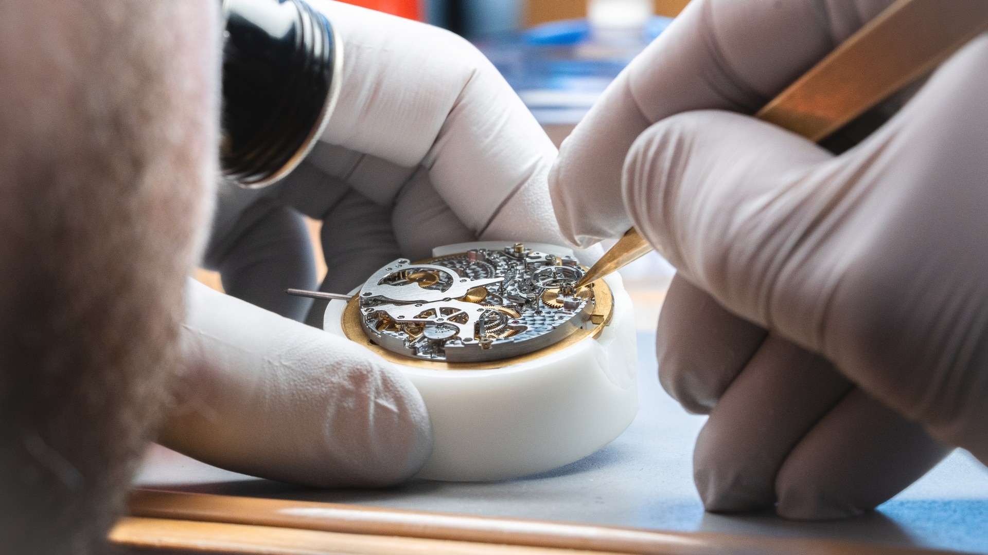 Gloved hands working on the intricate mechanism of a luxury watch.