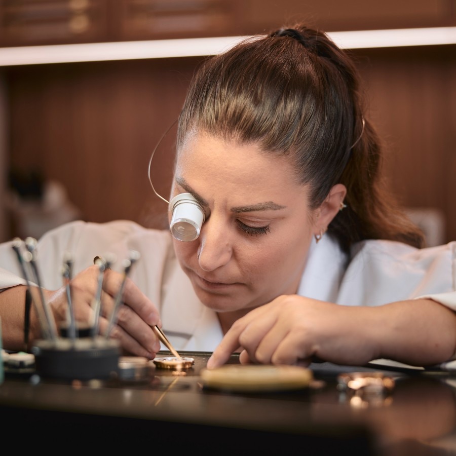 Watchmaker inspecting a mechanical movement through a loupe while adjusting it with a tool.