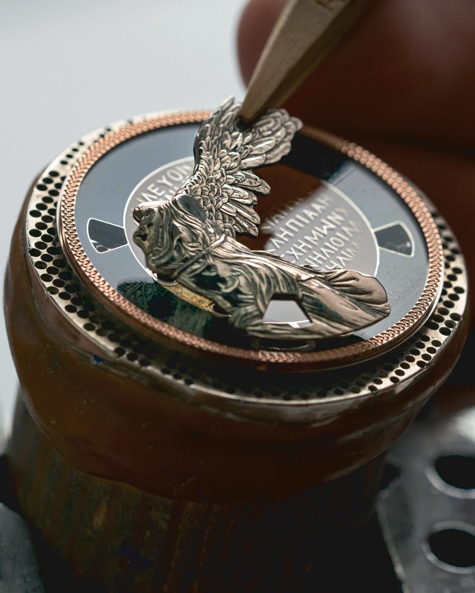 Watch dial featuring a winged figure being engraved in high relief.