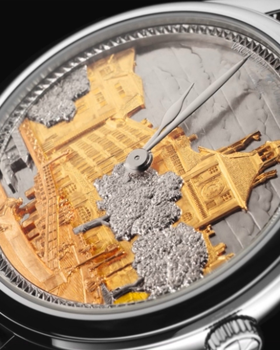 Close-up of a watch dial decorated with engraved and hand-painted architectural motifs in yellow and silver tones.