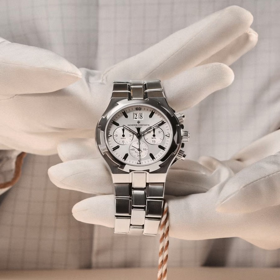 Gloved hands holding a stainless steel watch with a white dial.