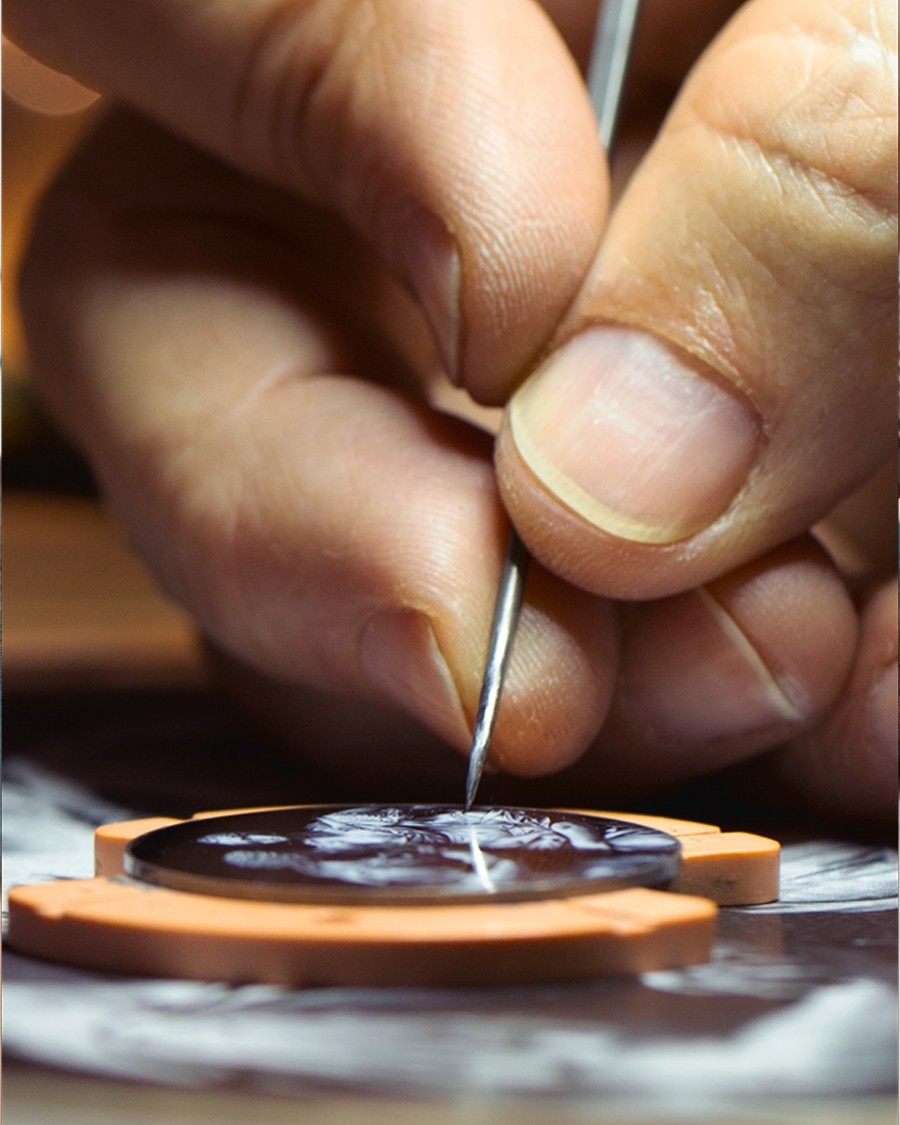 Close-up of a hand engraving fine details into a watch dial with a precision tool.