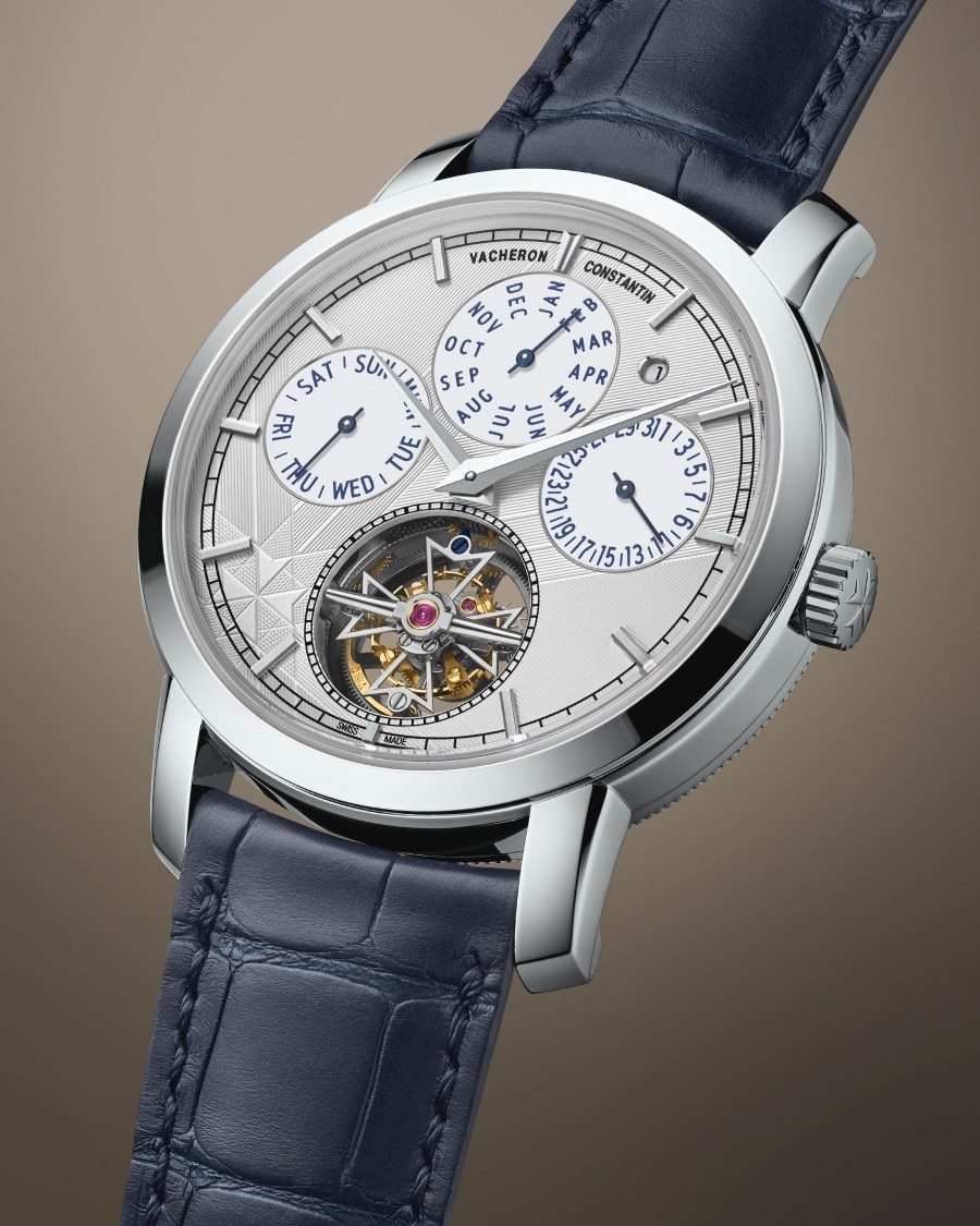 Traditionnelle - Tourbillon Ewiger Kalender Eine Uhr mit blauem Lederarmband, silbernem Gehäuse, mehreren Kalender-Hilfszifferblättern und freiliegendem Uhrwerk.