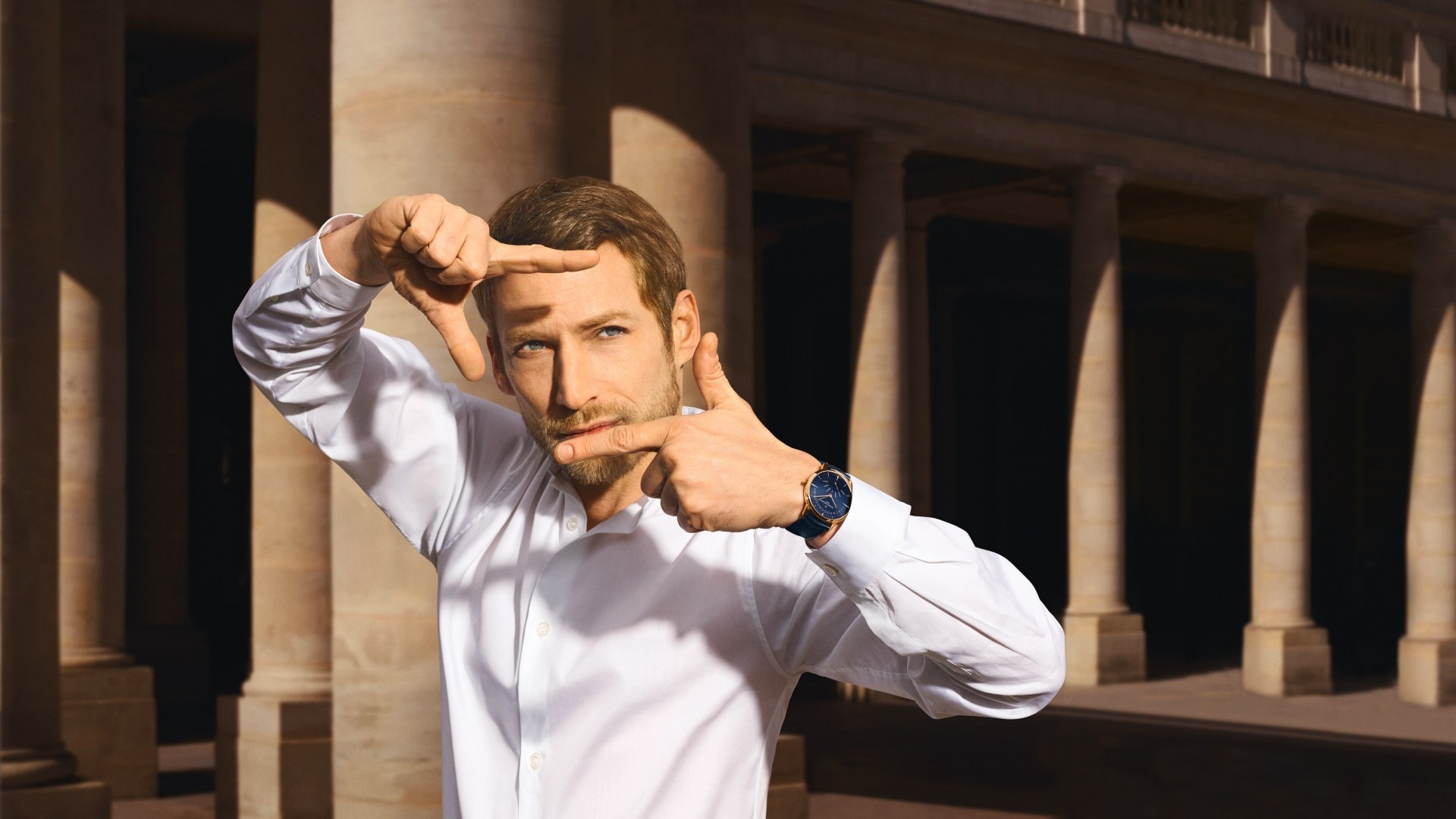 Man gesturing a frame with his hands in front of architectural columns.