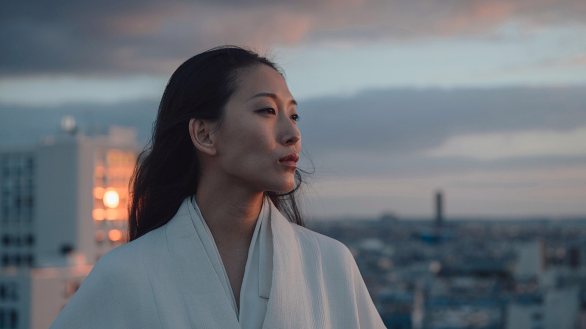 Portrait of a woman at dusk with a cityscape  in the background.