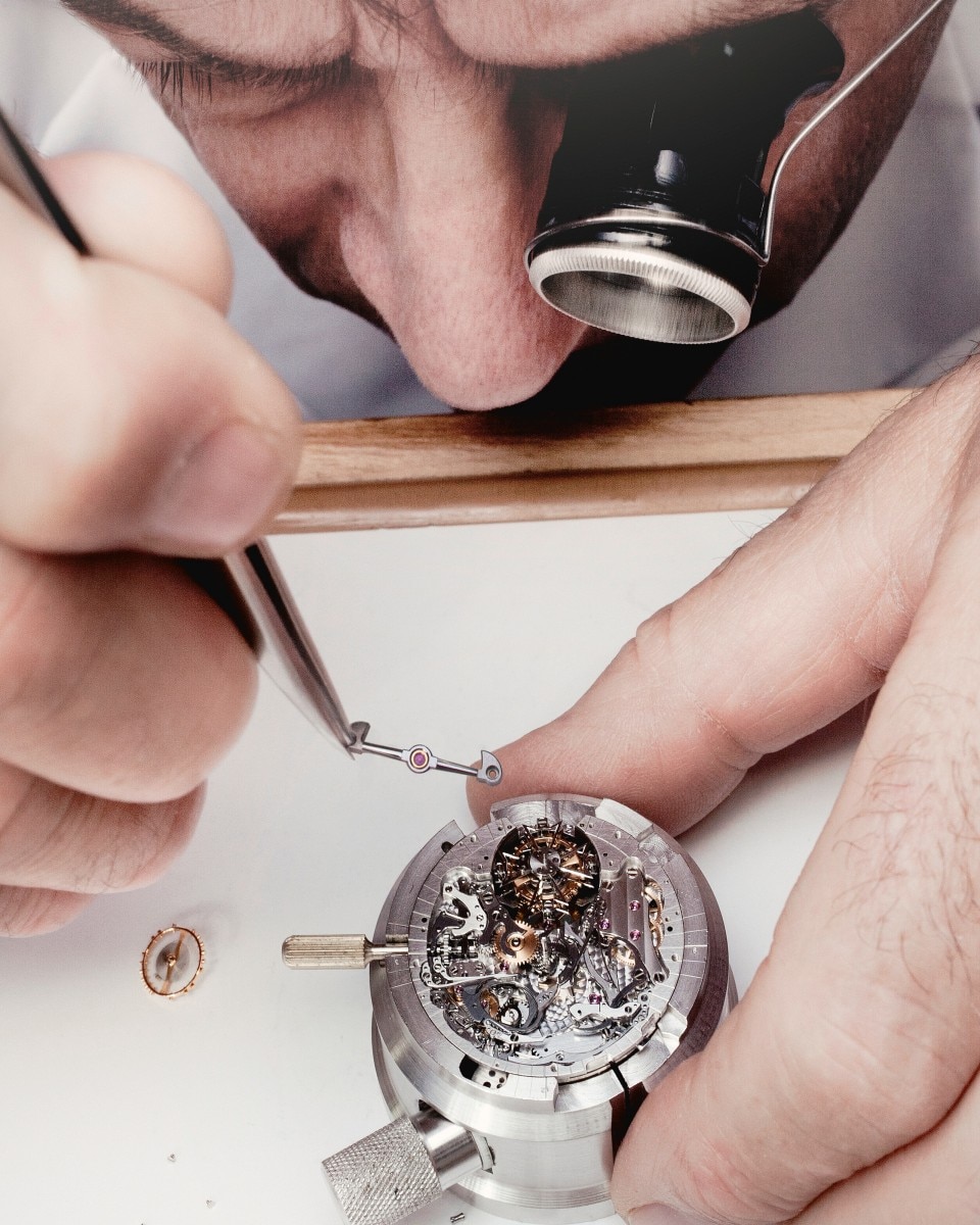 L’orologiaio usa delle pinzette per inserire un componente nel movimento meccanico.