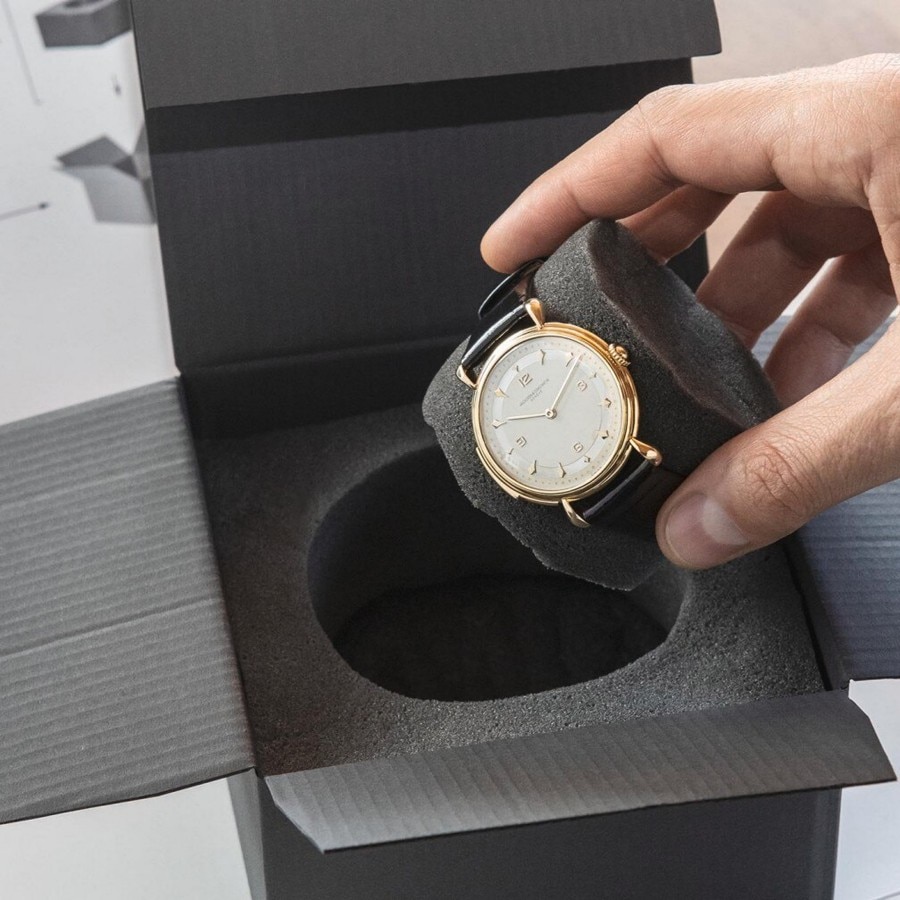 Hands opening a presentation box containing a gold wristwatch with a white dial.