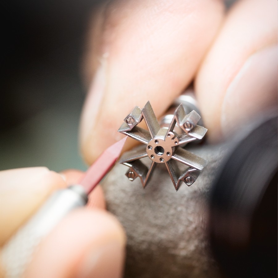 Artisan holding a small, finely crafted watch component with precision tweezers.