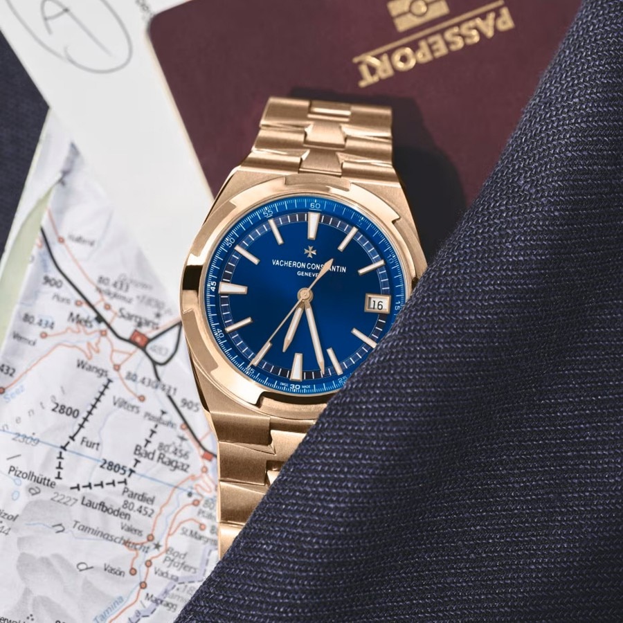 A powerful watch with a gold bracelet and a dark blue case leaning against a red passport and map