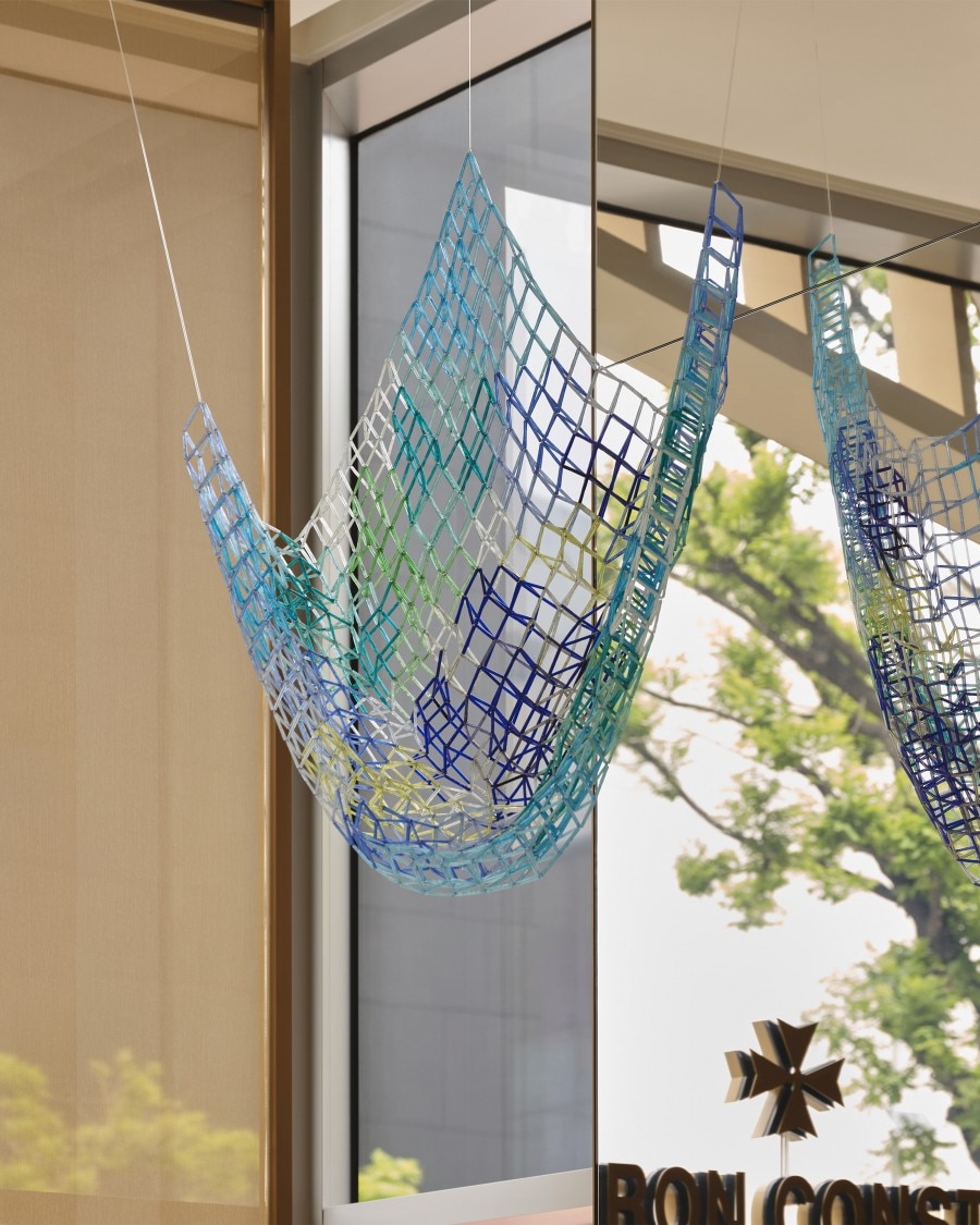A colorful, net-like sculpture hanging from the ceiling in front of a large window.