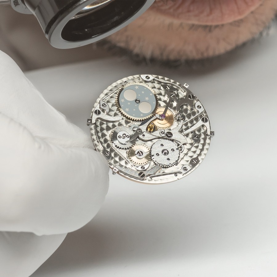 Watchmaker looking at a Traditionnelle watch caliber with a magnifying glass