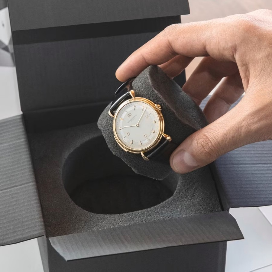Hand placing a gold watch into a foam insert inside a presentation box.