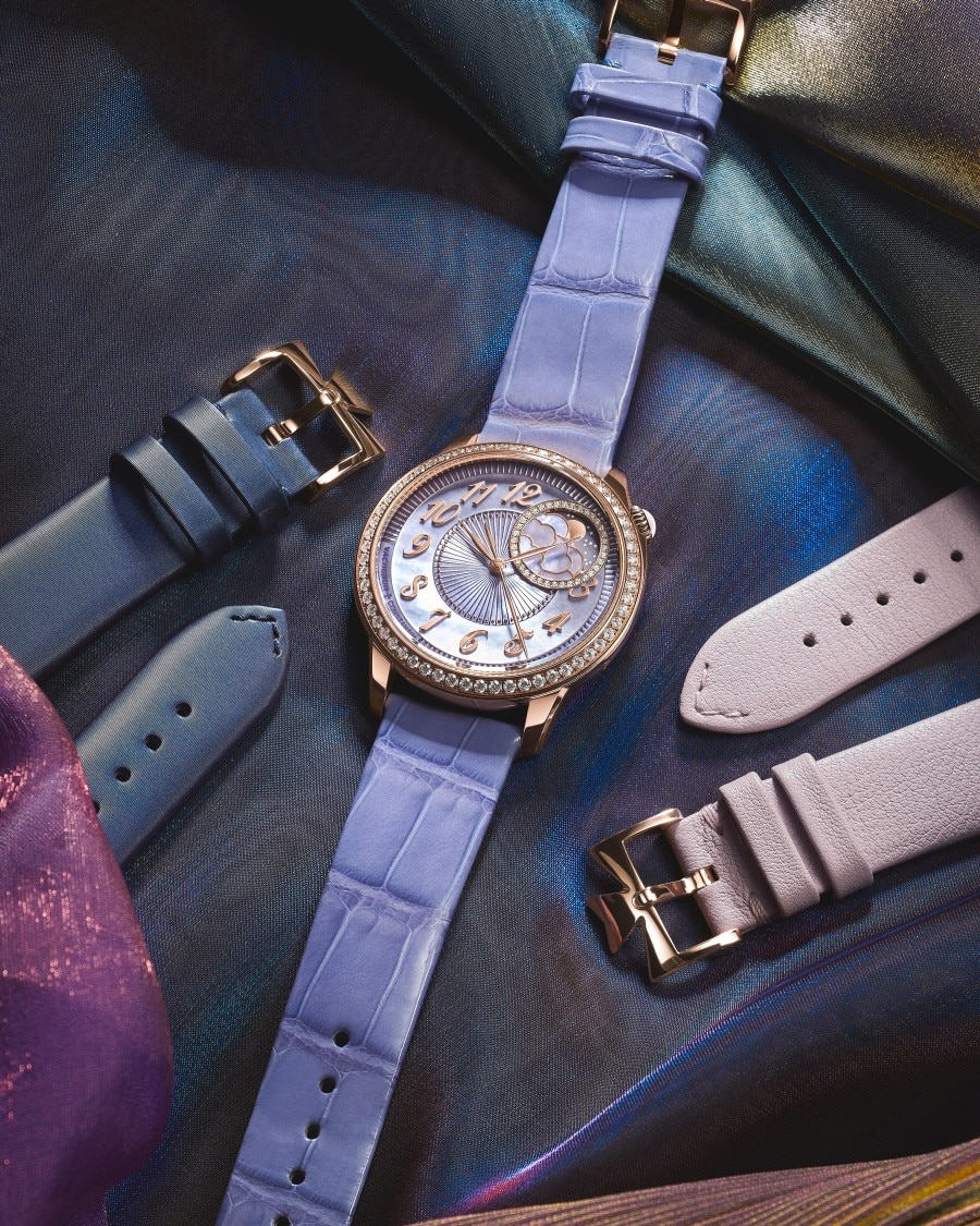Luxury watch with leather strap displayed on textured fabric, surrounded by additional strap options.