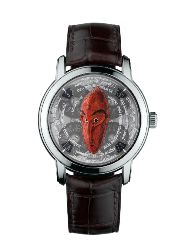 A silver wirstwatch with a black leather strap, featuring an artistic dial with a red tribal mask design and French text.