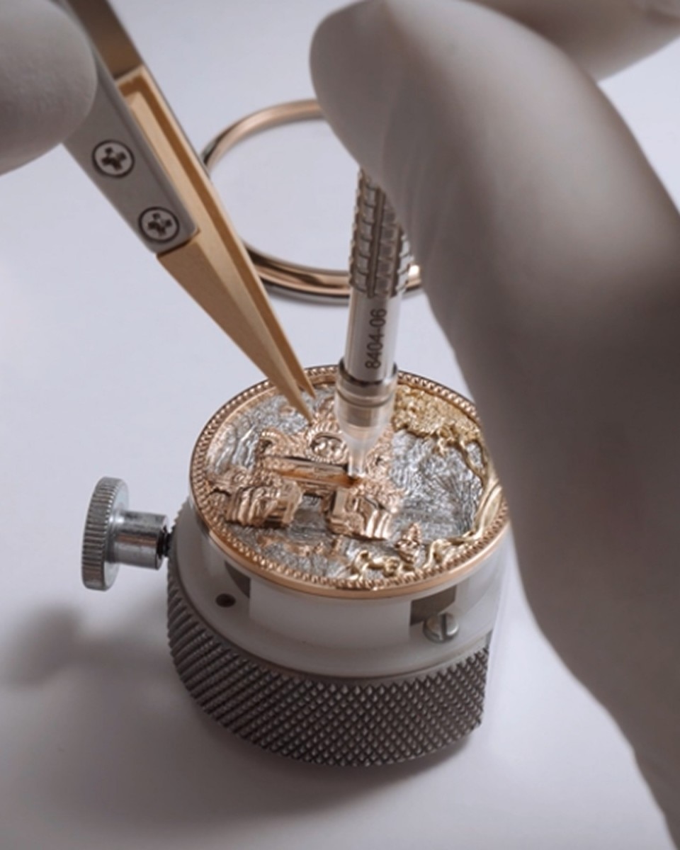 Watchmaker assembling a miniature sculpted scene on a watch dial using fine tools.