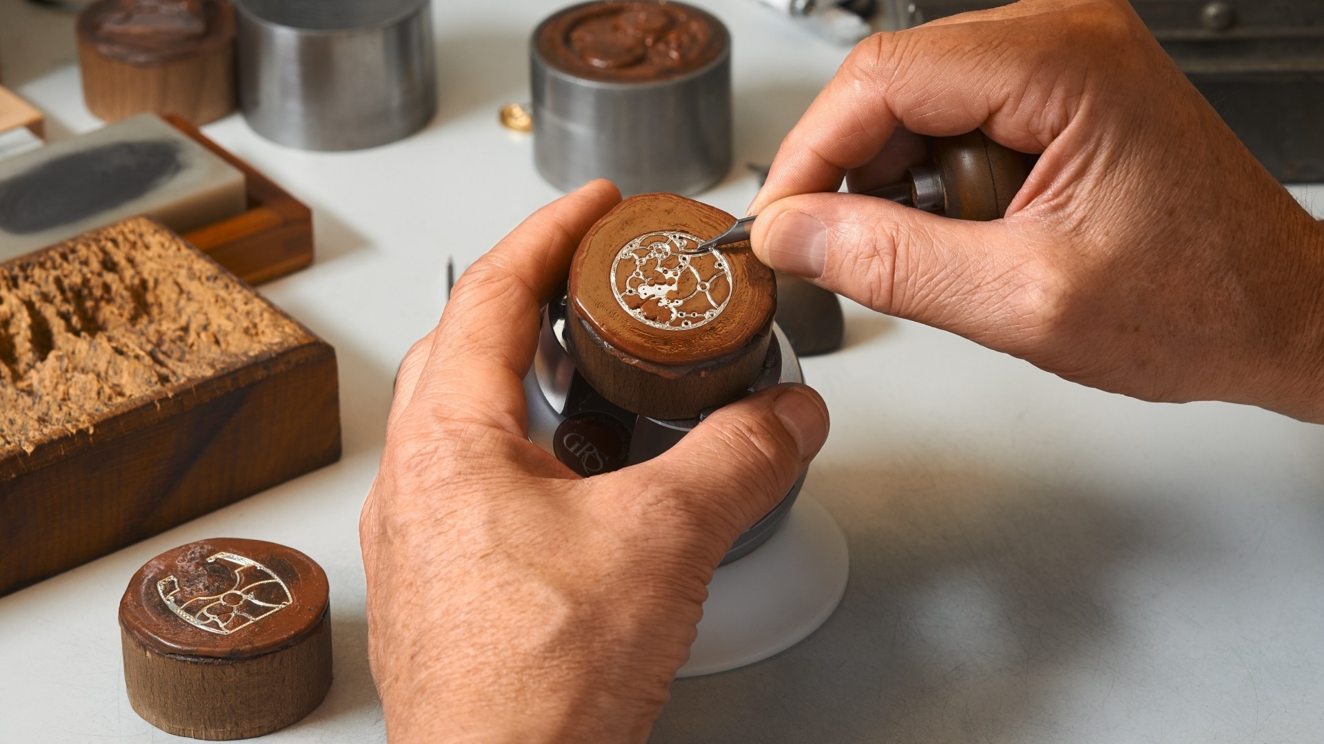 在小巧圆形金属表面之上，双手手工雕刻一枚装饰图案。