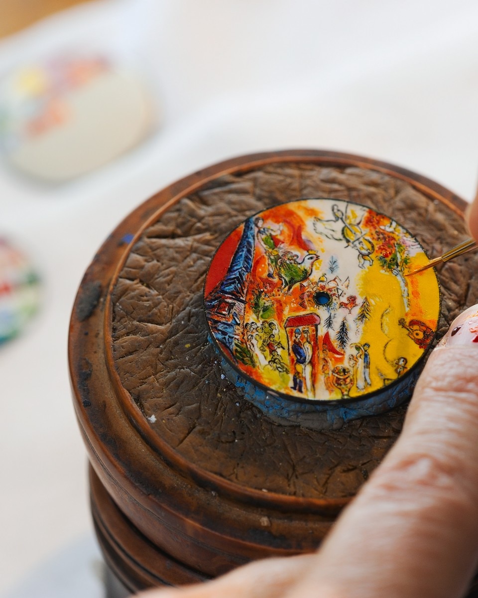 Miniature painted watch dial with a vivid countryside scene in yellow and red tones.