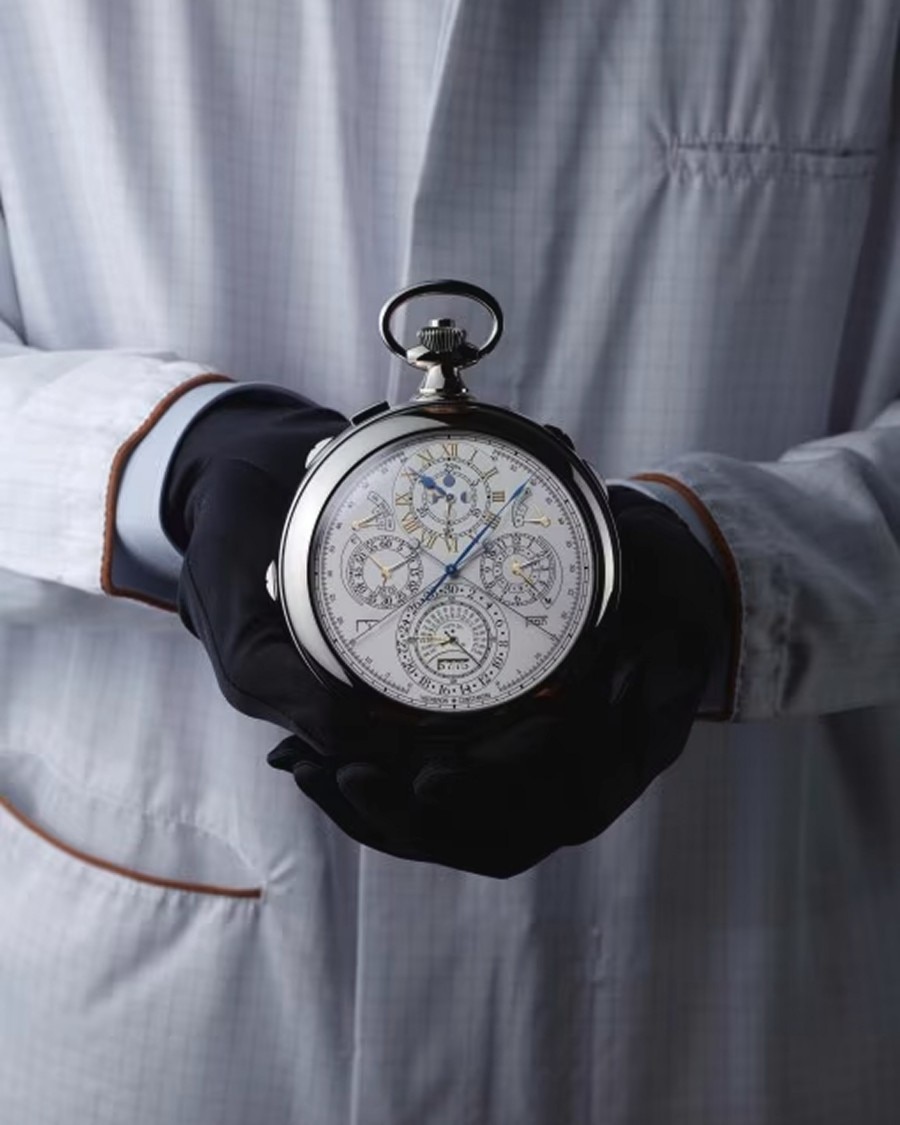 Les Cabinotiers Gloved hands holding a vintage  pocket watch against a white lab coat.