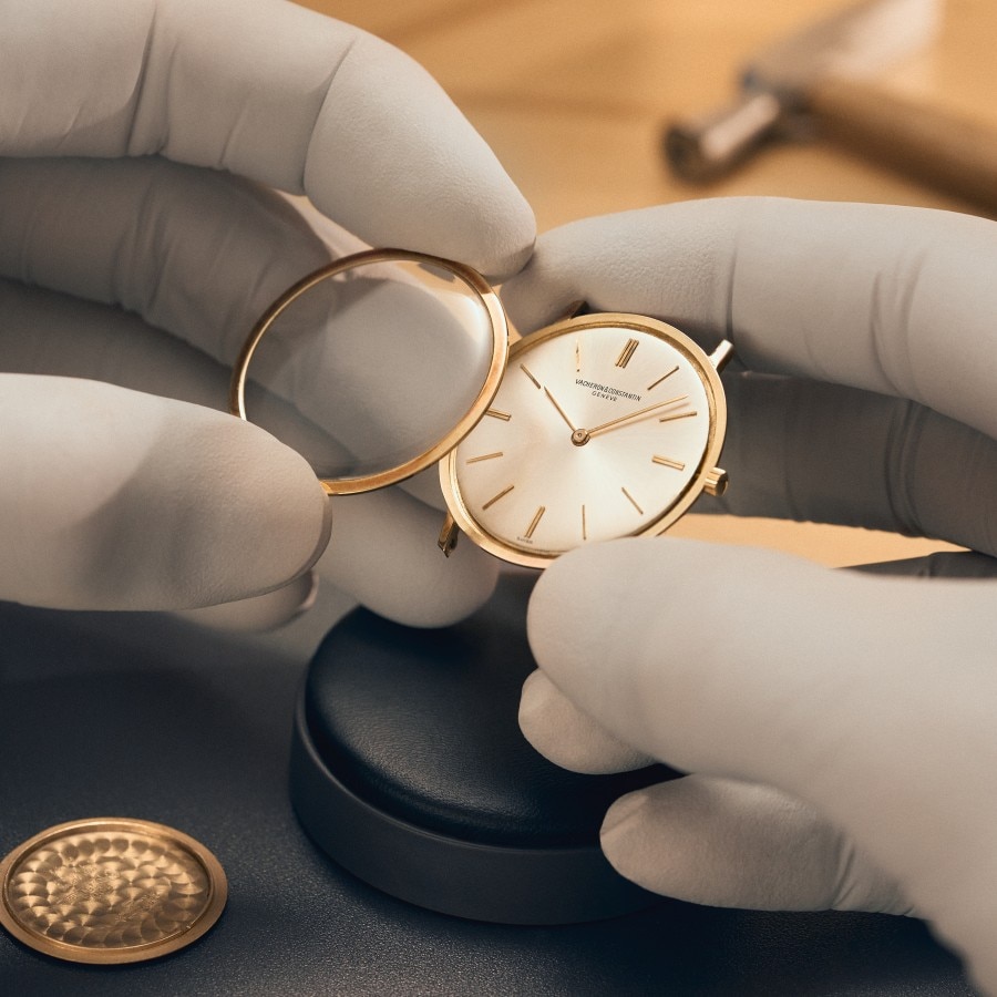 Gloved hands holding a stainless steel watch with a white dial.