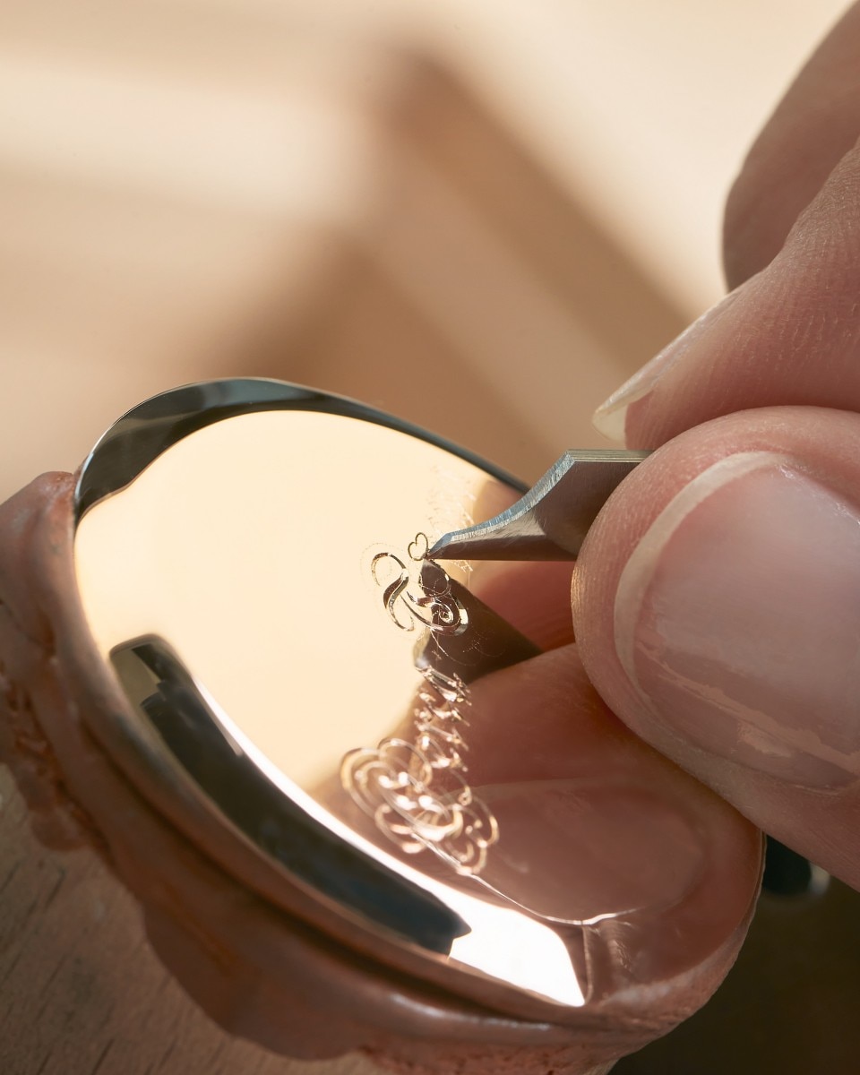 Close-up of a craftaman engraving fine details on a polished watch case.
