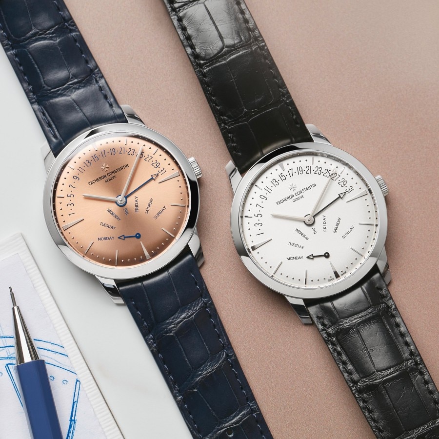 Two Patrimony watches, one with a salmon-toned dial and dark blue strap, one with a white dial and black strap.