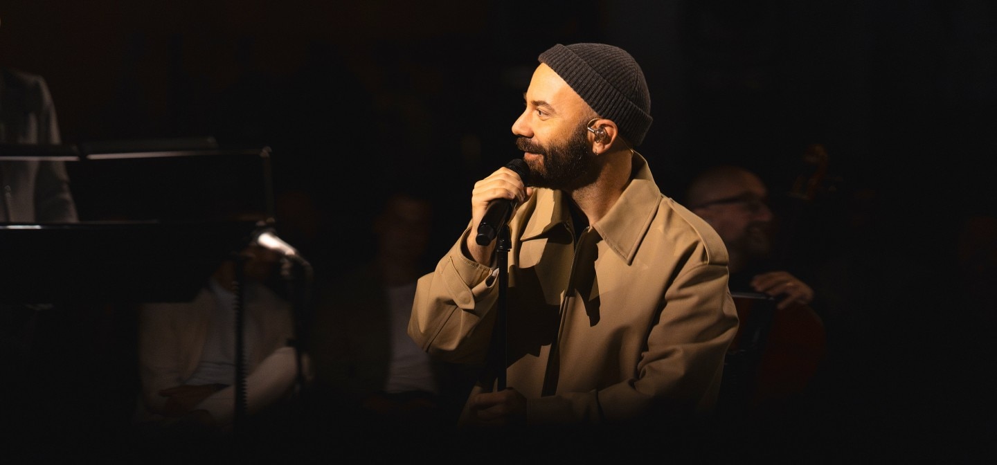 Woodkidholding a microphone and wearing a beanie and coat, performing on stage.