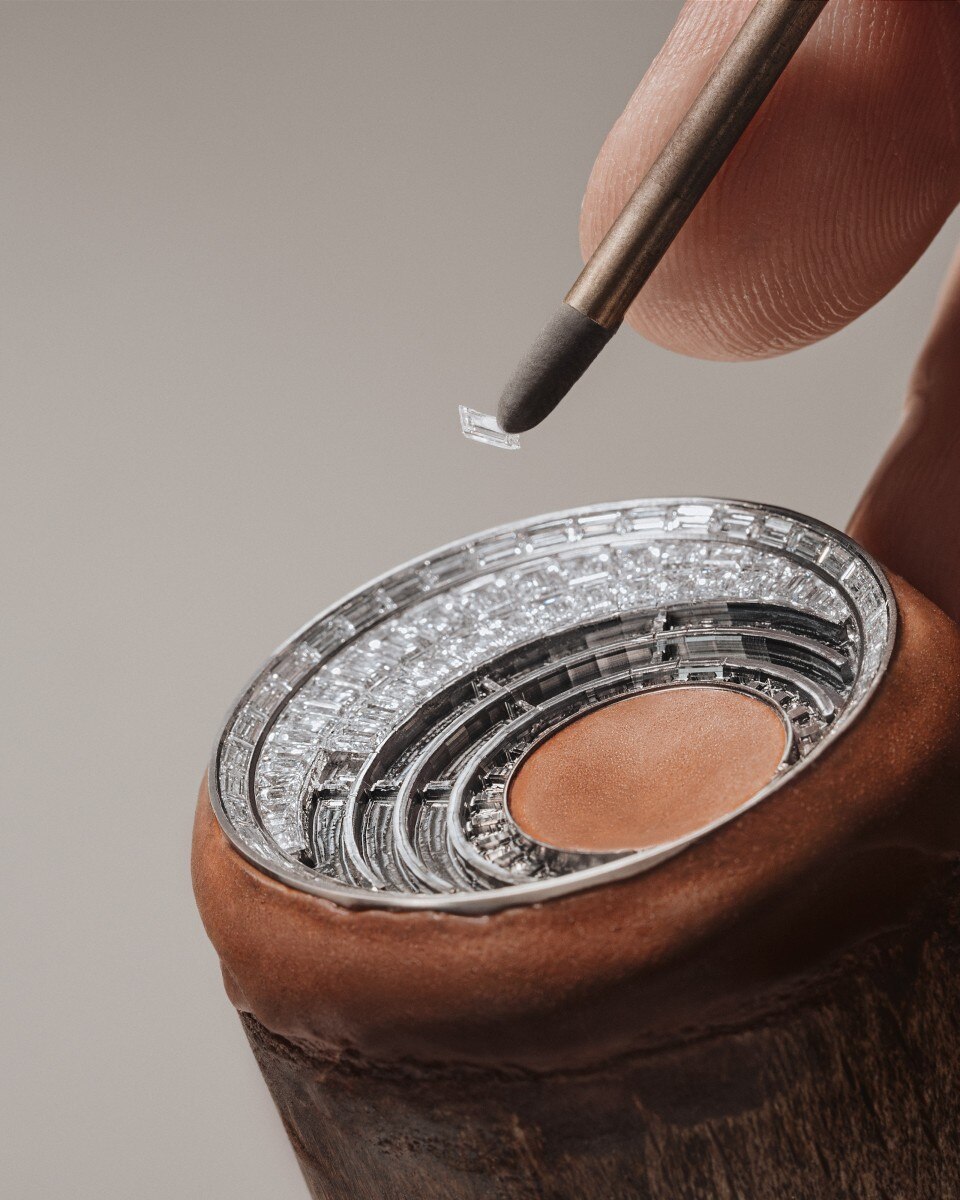 Artisan placing a baguette-cut diamond into a circular pave setting on a watch dial.