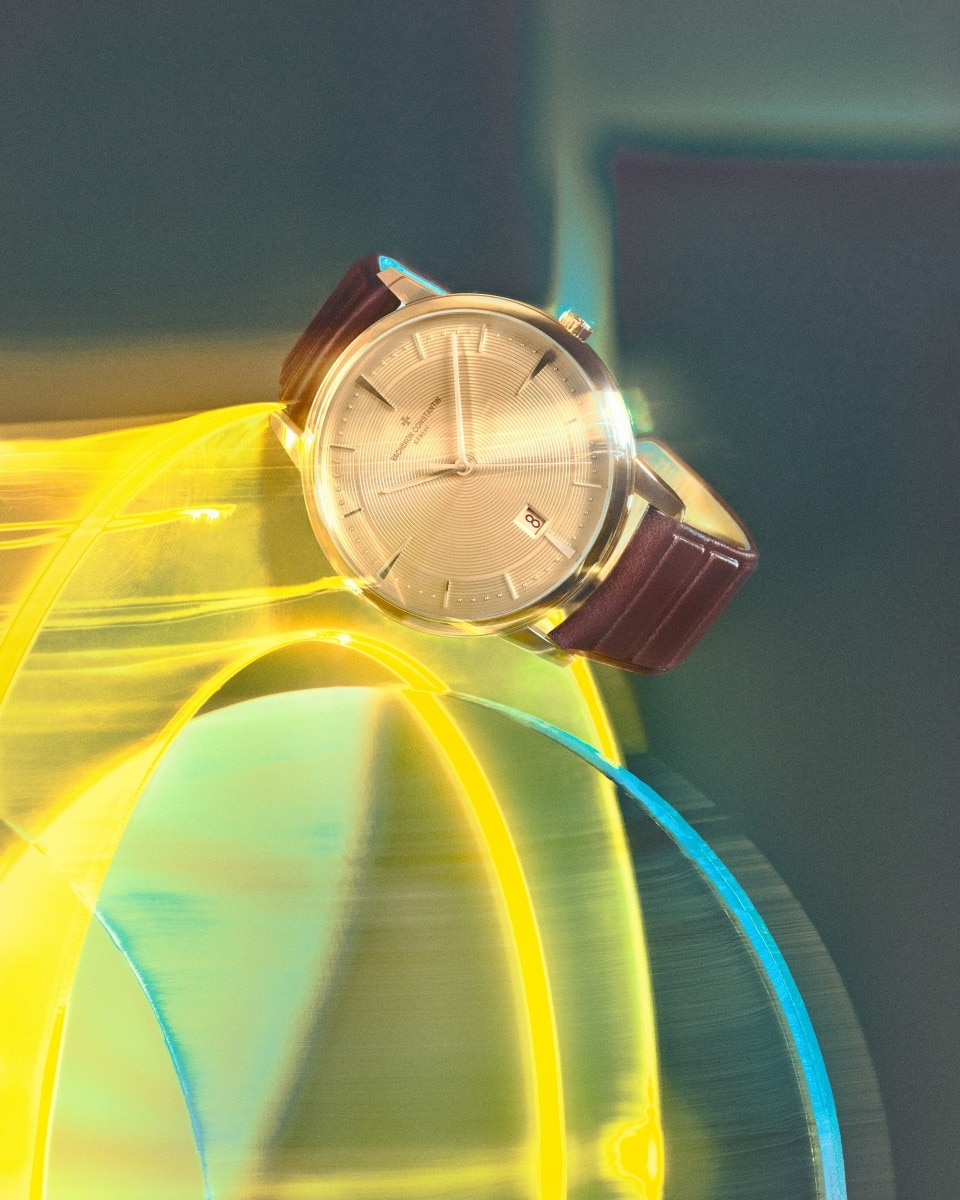 A gold watch with brown leather strap displayed against a dynamic yellow and green background.