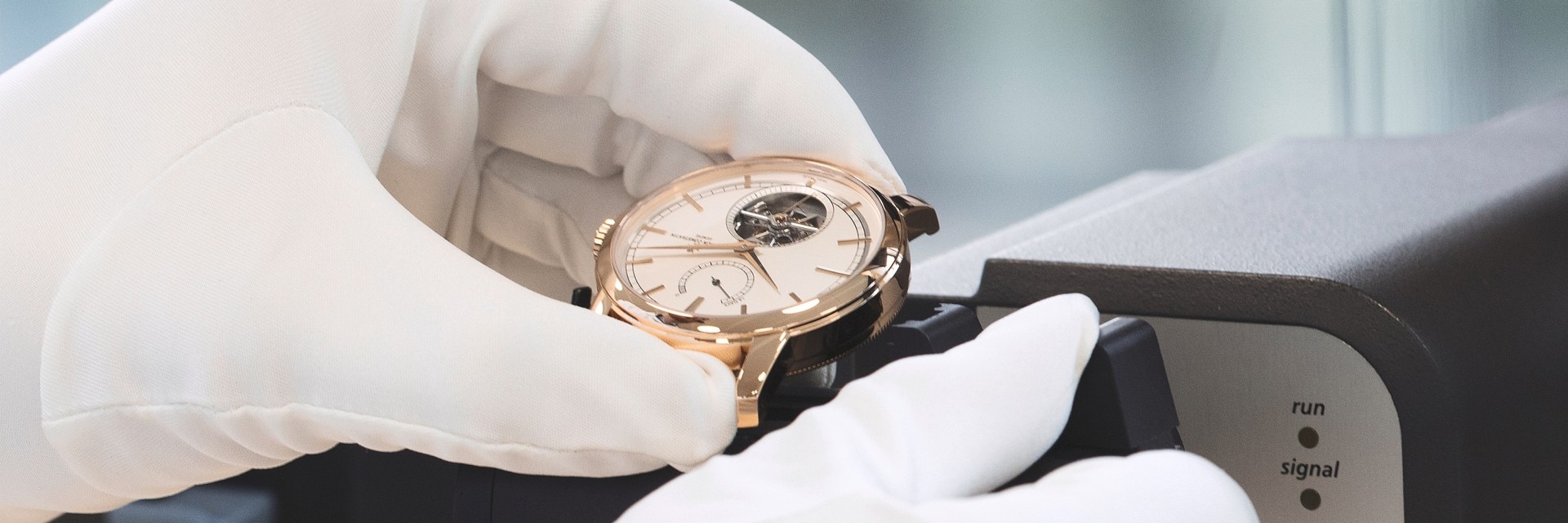 Des mains gantées tenant une montre Vacheron Constantin avec fond ouvert, inspectant son mouvement mécanique complexe.