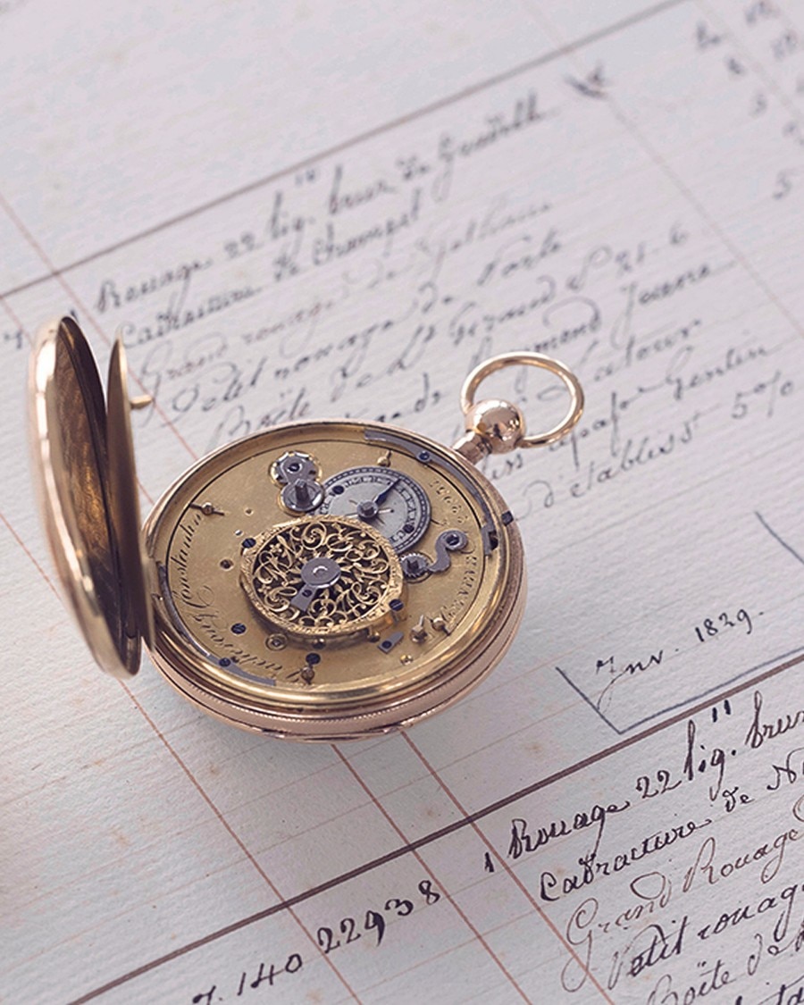 Open gold pocket watch revealing inner mechanical movement, placed on handwritten documents.