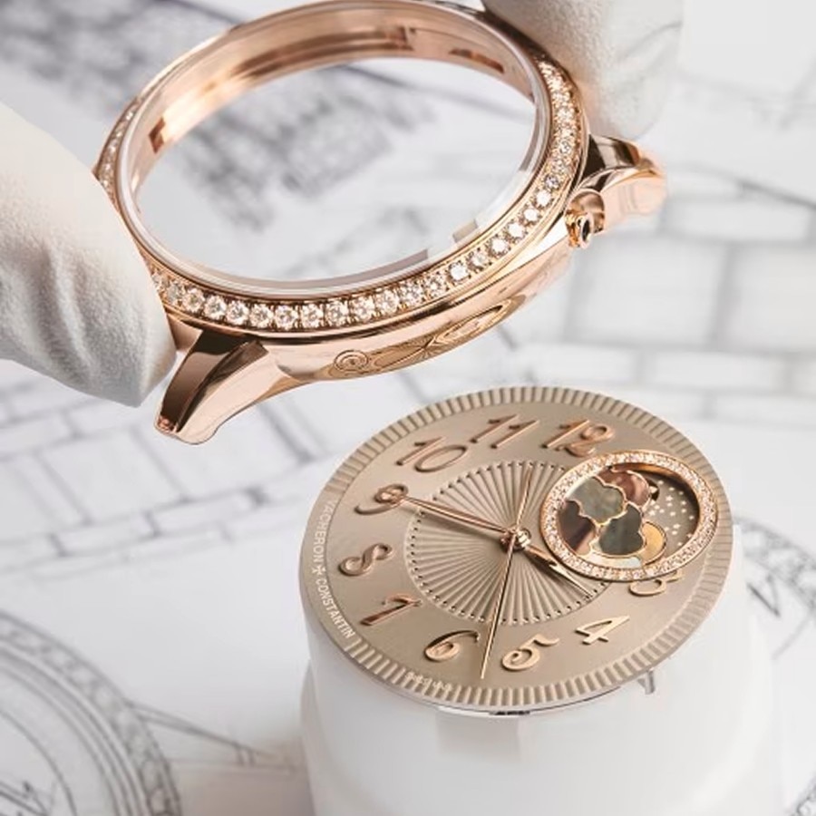 Close-up of a hand in white gloves placing a round gold watch bezel on a case with a gold details