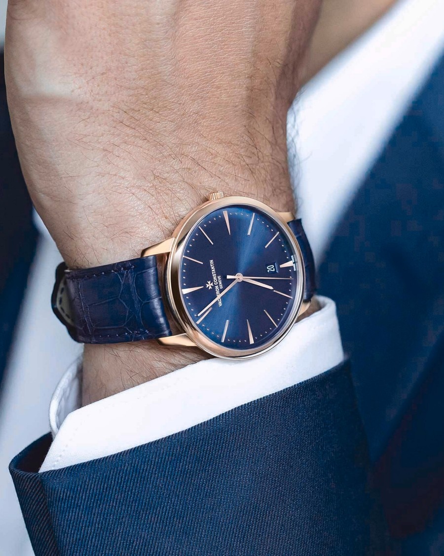 Close-up of a man's hand in a navy suit wearing a watch with a navy case and a leather strap and with a gold details