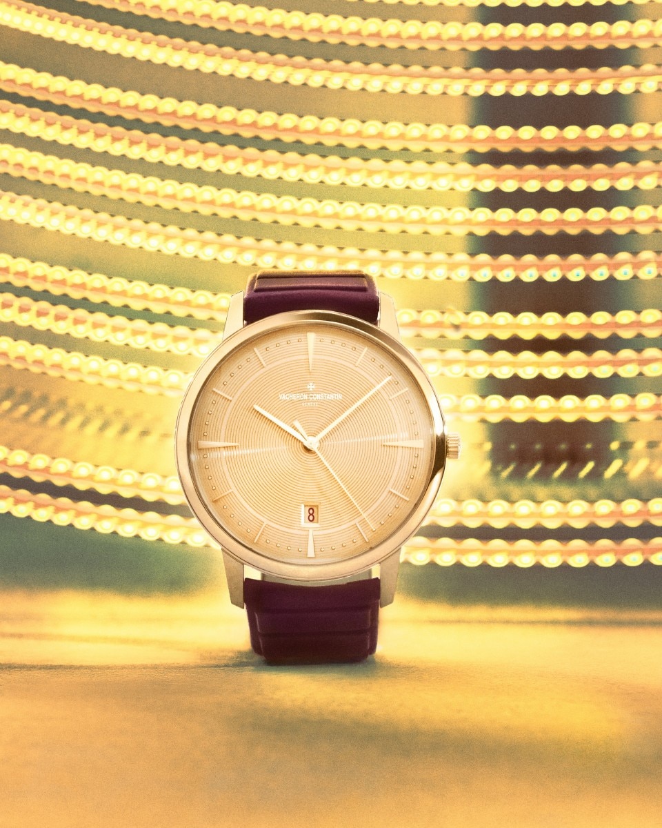 A close-up of a gold watch with a brown leather strap, set against an abstract yellow background.